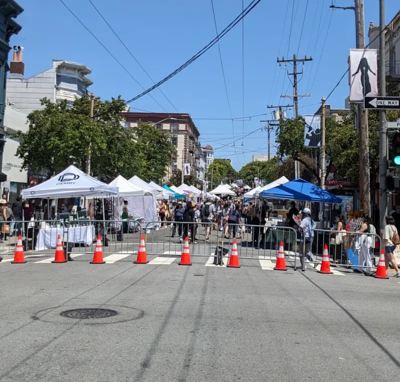 Vendor tents, barricades, and crowds along a closed street at a San Francisco community festival