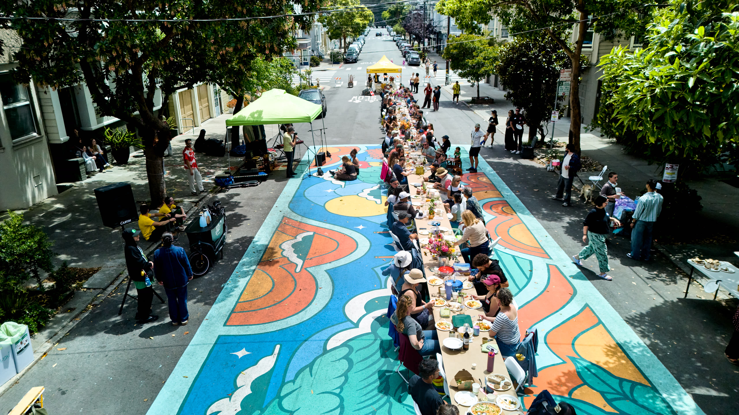 Aerial view of a long communal potluck table lined with guests running down Lyon Street in San Francisco